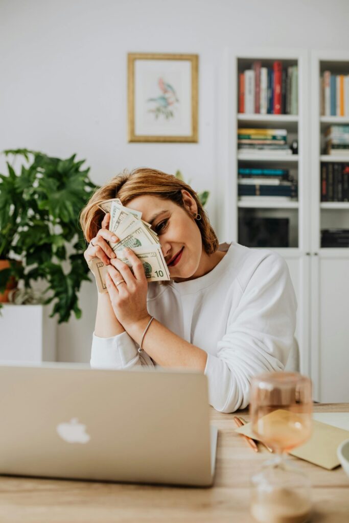 Woman Sitting in Front of Her Laptop and Holding a Lot of Cash for Compensation Consulting Services