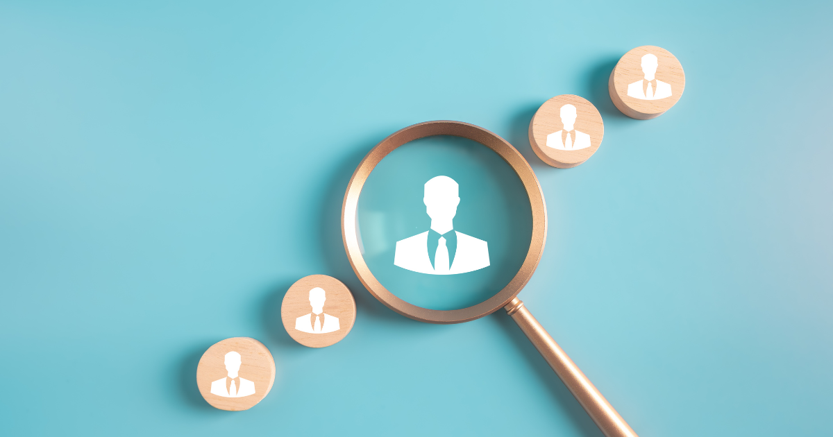 Magnifying glass over a row of wooden avatar tokens, illustrating candidate search and recruitment