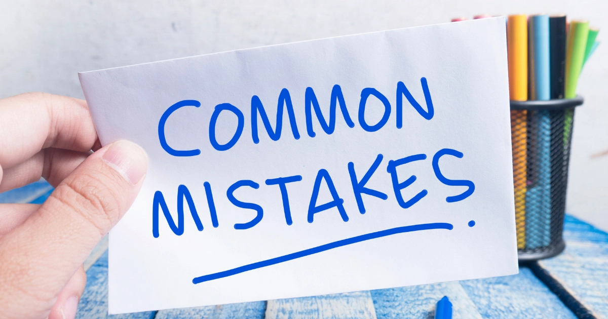 Card held by a hand reading 'Common Mistakes' in blue handwriting; background shows a pencil holder.